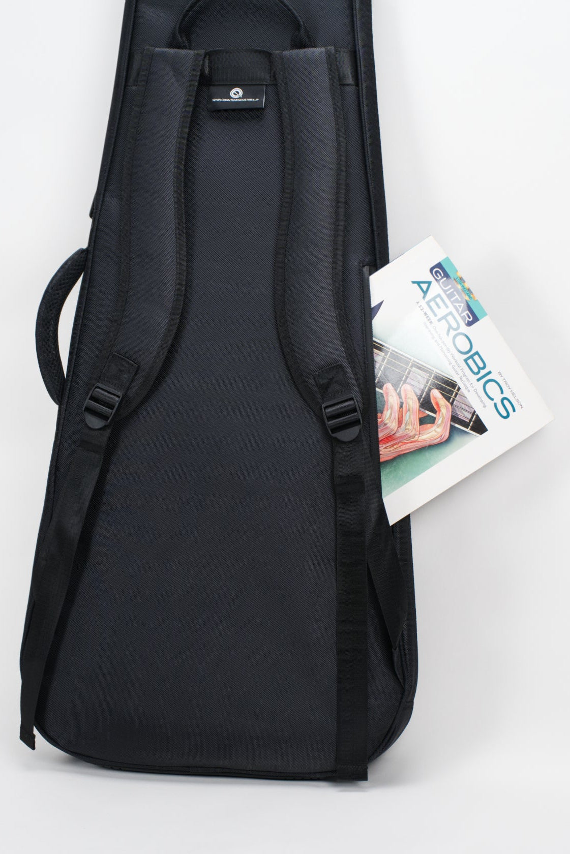 A black padded carrying case or bag with shoulder straps, shown upright against a light gray studio background. A magazine or booklet is tucked into one side pocket.