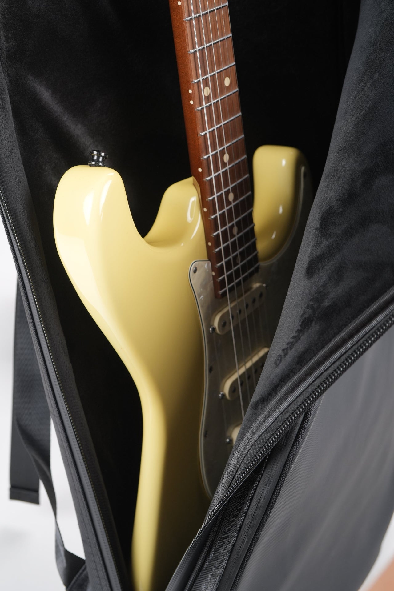 A cream-colored electric guitar tucked inside a black guitar bag with a plush black interior.