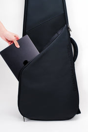 A black guitar gig bag with a hand placing a black laptop into its side laptop compartment, shown against a plain white studio background.