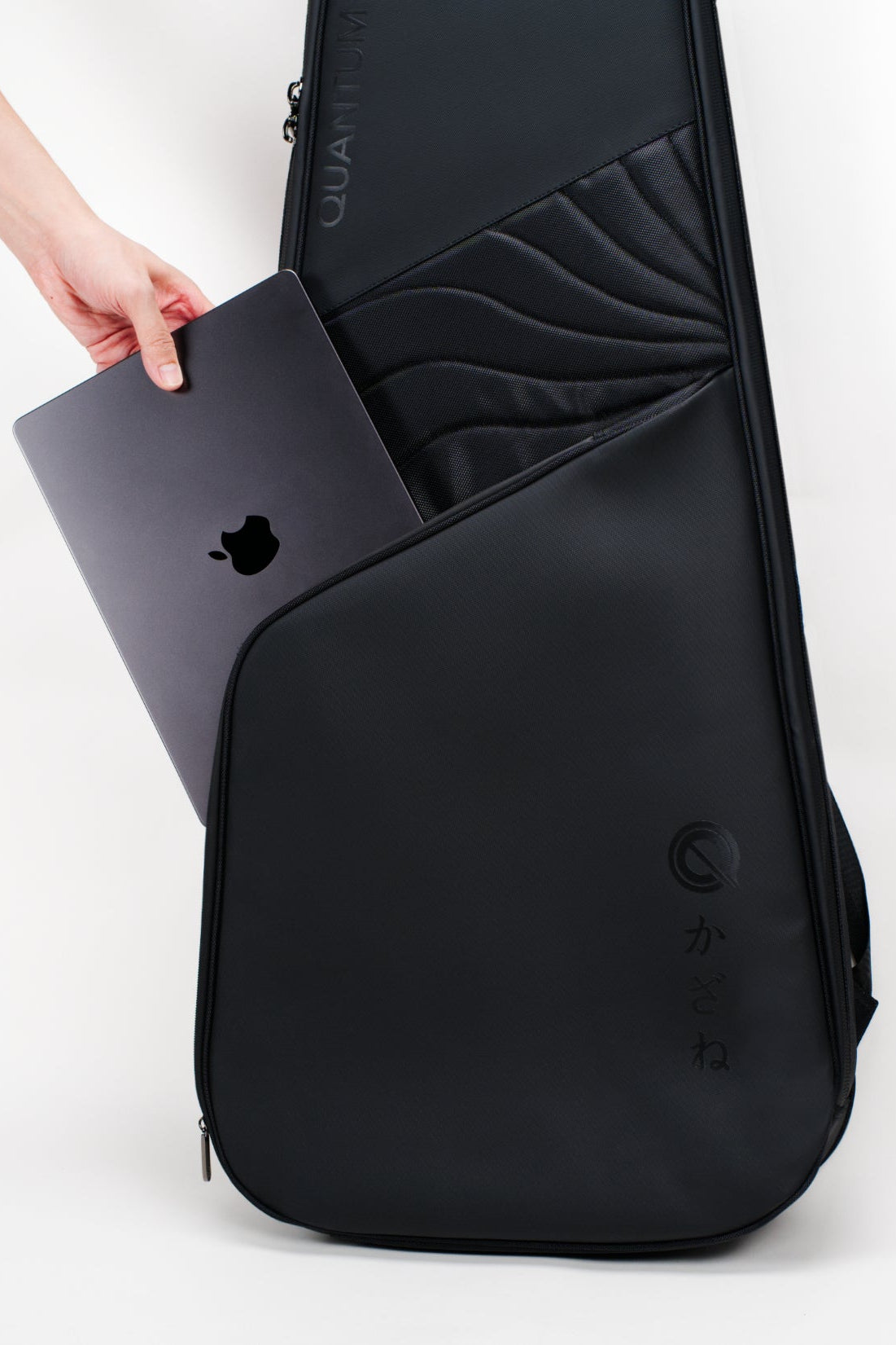 A black laptop backpack shown on a white studio background, with a hand inserting a dark gray laptop into its side pocket. The backpack features a sleek, modern design with a subtle wave pattern on the upper section and a circular logo near the bottom.